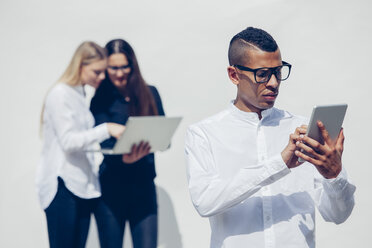 Porträt eines jungen Mannes mit Brille, der ein Mini-Tablet vor einem weißen Hintergrund benutzt - CHAF001172