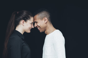 Glückliches junges Paar von Angesicht zu Angesicht vor einem schwarzen Hintergrund - CHAF001202