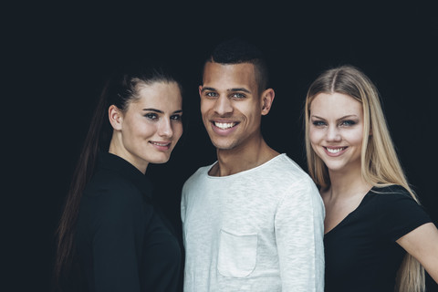 Gruppenbild von zwei jungen Frauen und einem jungen Mann vor einem schwarzen Hintergrund, lizenzfreies Stockfoto