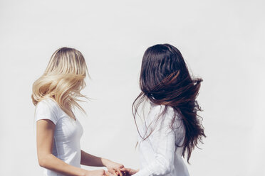 Zwei junge Frauen in weißer Kleidung werfen ihr Haar vor weißem Hintergrund - CHAF001219