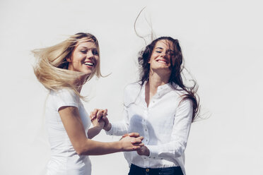 Zwei junge Frauen halten sich an den Händen und werfen ihr Haar vor einem weißen Hintergrund - CHAF001221