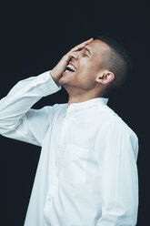 Laughing young woman with hand on his face wearing white shirt in front of black background - CHAF001240