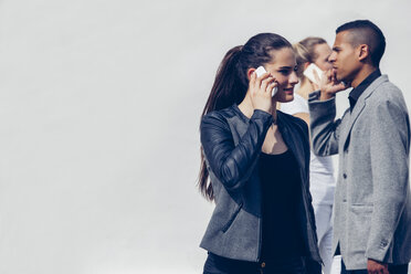 Young woman telephoning with smartphone in front of two other people - CHAF001258