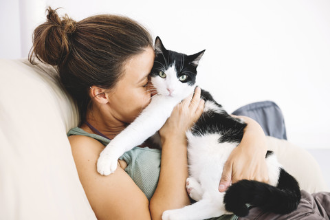 Frau, die auf dem Sofa sitzt und ihre Katze umarmt, lizenzfreies Stockfoto