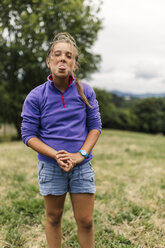 Portrait of girl standing on a meadow sticking out tongue - MGOF000414