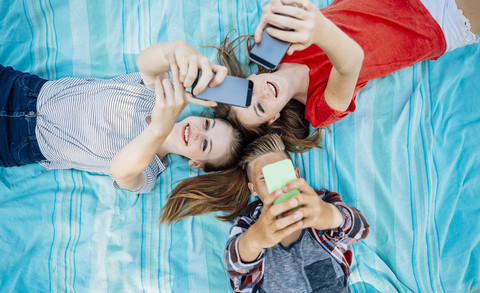 Drei jugendliche Freunde mit Smartphones auf einer Decke liegend, lizenzfreies Stockfoto