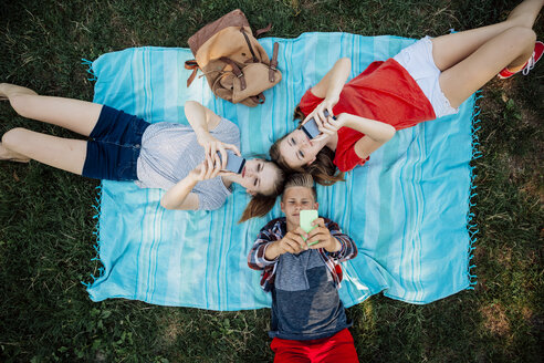 Three teenage friends with smartphones lying on blanket - AIF000066