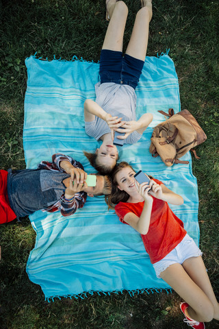 Three teenage friends with smartphones lying on blanket stock photo
