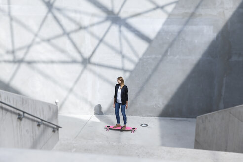 Businesswoman with pink skateboard in modern architecture - FMKF001735