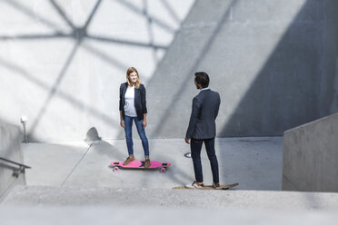 Two business people standing on skateboards in modern architecture - FMKF001737