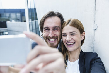 Portrait of two laughing business people taking a selfie with smartphone - FMKF001743
