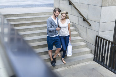 Deutschland, Köln, junges Pärchen schaut auf Smartphone, geht eine Treppe hinunter - FMKF001756