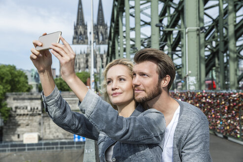 Deutschland, Köln, junges Paar macht ein Selfie mit Smartphone an der Hohenzollernbrücke - FMKF001768