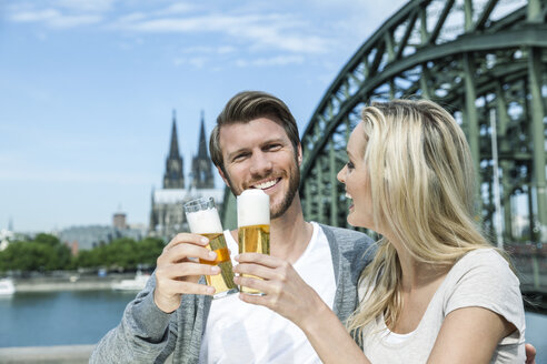 Deutschland, Köln, glückliches junges Paar stößt mit Kölschgläsern vor dem Rhein an - FMKF001771