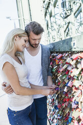 Germany, Cologne, young couple looking at love locks on Hohenzollern Bridge - FMKF001774