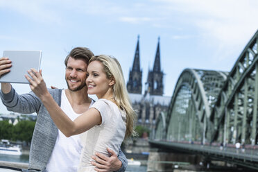 Germany, Cologne, smiling young couple taking a selfie with digital tablet - FMKF001793