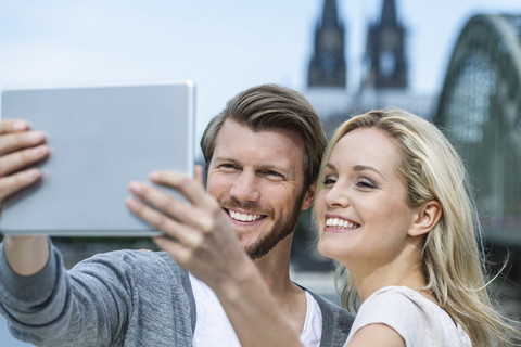 Germany, Cologne, portrait of smiling young couple taking a selfie with digital tablet stock photo