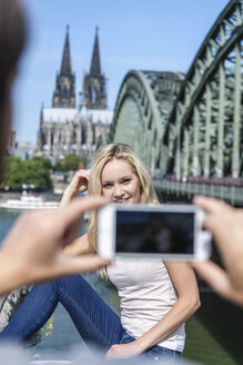 Deutschland, Köln, junger Mann fotografiert seine Freundin mit Smartphone - FMKF001801