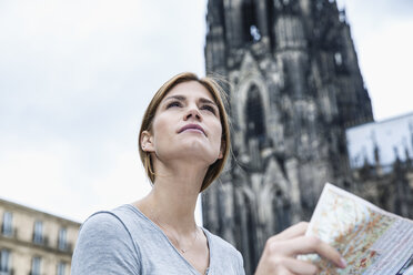 Deutschland, Köln, Porträt einer jungen Frau mit Stadtplan vor dem Kölner Dom - FMKF001805