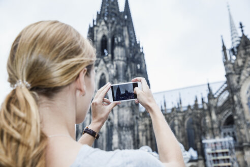 Deutschland, Köln, junge Frau fotografiert den Kölner Dom mit Smartphone - FMKF001806