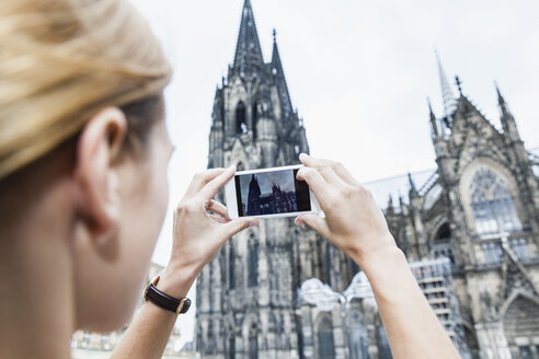 Deutschland, Köln, junge Frau fotografiert den Kölner Dom mit Smartphone - FMKF001807