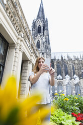 Deutschland, Köln, junge Frau macht ein Selfie mit Smartphone vor dem Kölner Dom - FMKF001824