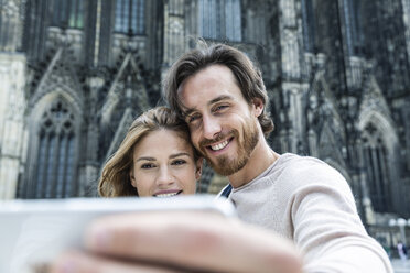 Germany, Cologne, portrait of young couple taking a selfie in front of Cologne Cathedral - FMKF001826