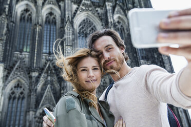 Germany, Cologne, portrait of young couple taking a selfie in front of Cologne Cathedral - FMKF001827