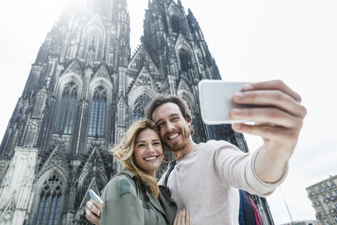 Germany, Cologne, portrait of young couple taking a selfie in front of Cologne Cathedral - FMKF001828