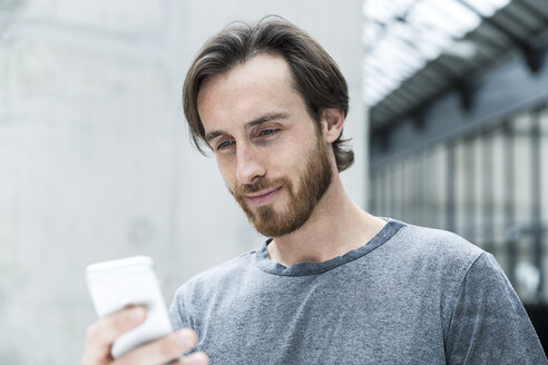 Porträt eines jungen Mannes, der auf sein Smartphone schaut - FMKF001829