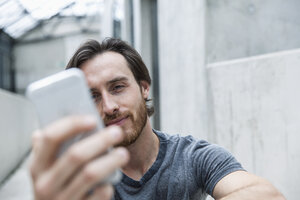 Porträt eines jungen Mannes, der auf sein Smartphone schaut - FMKF001831