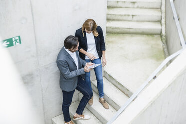 Zwei Geschäftsleute stehen auf einer Treppe und schauen auf ein digitales Tablet - FMKF001833