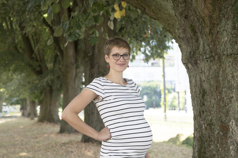 Porträt einer lächelnden schwangeren Frau mit Hand in der Hüfte in einem gestreiften Kleid, lizenzfreies Stockfoto