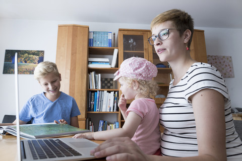 Schwangere Frau mit Sohn und kleiner Tochter zu Hause am Laptop, lizenzfreies Stockfoto