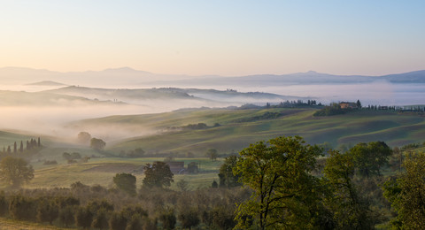 Italien, Toskana, Val d'Orcia, Blick auf hügelige Landschaft bei Sonnenaufgang im Nebel, lizenzfreies Stockfoto