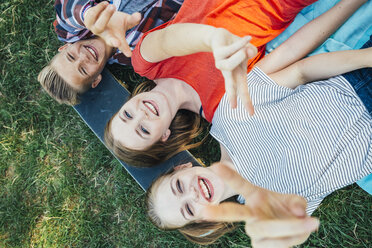 Three happy teenage friends lying on skateboard in meadow making victory sign - AIF000069
