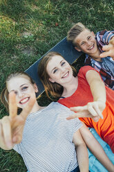 Drei glückliche Teenager-Freunde liegen auf einem Skateboard auf einer Wiese und machen ein Siegeszeichen - AIF000071