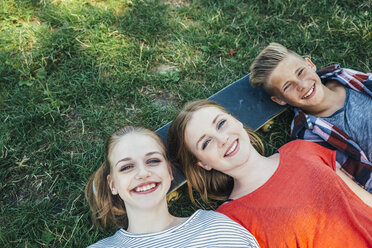 Three happy teenage friends lying on skateboard in meadow - AIF000074