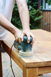 Man sanding an oak table with a random orbital sander - HAWF000823