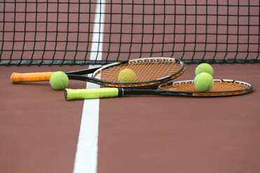 Zwei Tennisschläger und vier Bälle liegen auf dem Boden des Tennisplatzes - MGOF000447