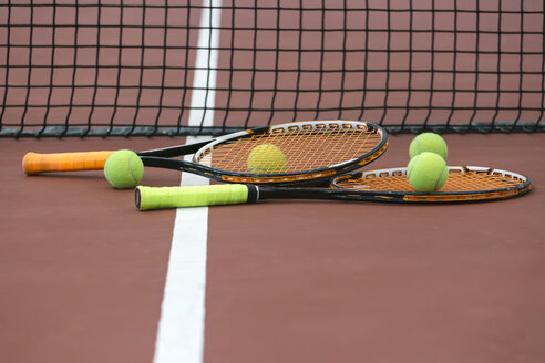 Zwei Tennisschläger und vier Bälle liegen auf dem Boden des Tennisplatzes - MGOF000447