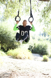 Mann macht CrossFit-Übung an Ringen, die an einem Baumstamm hängen - MAEF010836