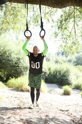Man doing CrossFit exercise on rings hanging on tree trunk - MAEF010839