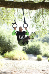 Man doing CrossFit exercise on rings hanging on tree trunk - MAEF010840