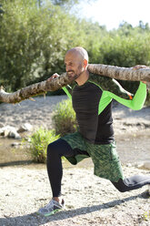 Man doing CrossFit exercise with tree trunk on his shoulders - MAEF010846