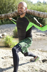 Man doing CrossFit exercise with tree trunk on his shoulders - MAEF010849