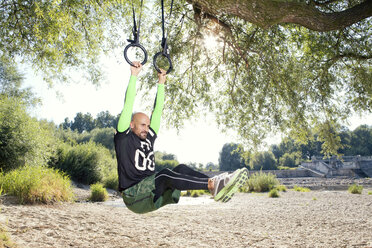 Mann macht CrossFit-Übung an Ringen, die an einem Baumstamm hängen - MAEF010855