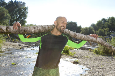 Smiling man doing CrossFit exercise with tree trunk on his shoulders - MAEF010857