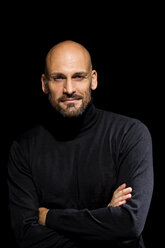 Portrait of man with crossed arms wearing black turtleneck in front of black background - MAEF010885