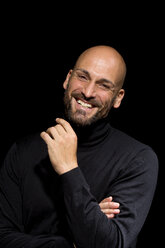 Porträt eines lachenden Mannes mit schwarzem Rollkragenpullover vor einem schwarzen Hintergrund - MAEF010887
